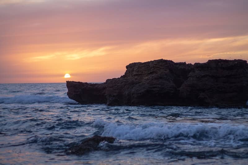 A sunset over the ocean with a rock formation in the foreground