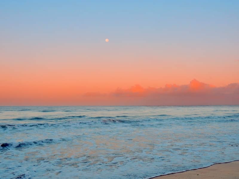 The sun is setting over the ocean on the beach