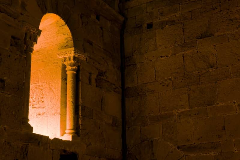 A light shines through a window in a stone building