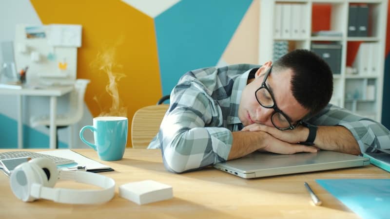 Man sleeping at desk with coffee and laptop.