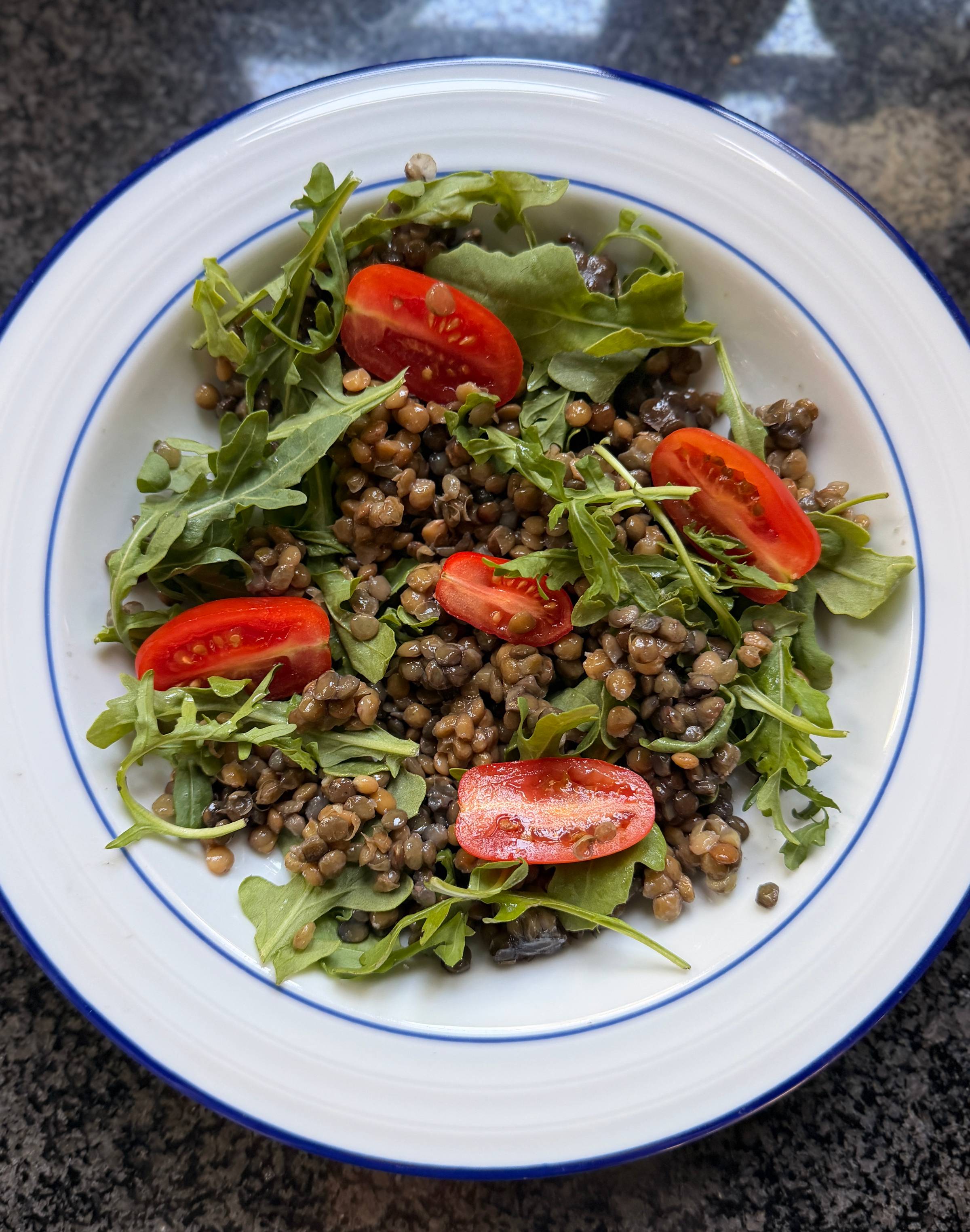 Fresh green salad topped with cherry tomatoes in a blue-rimmed white bowl