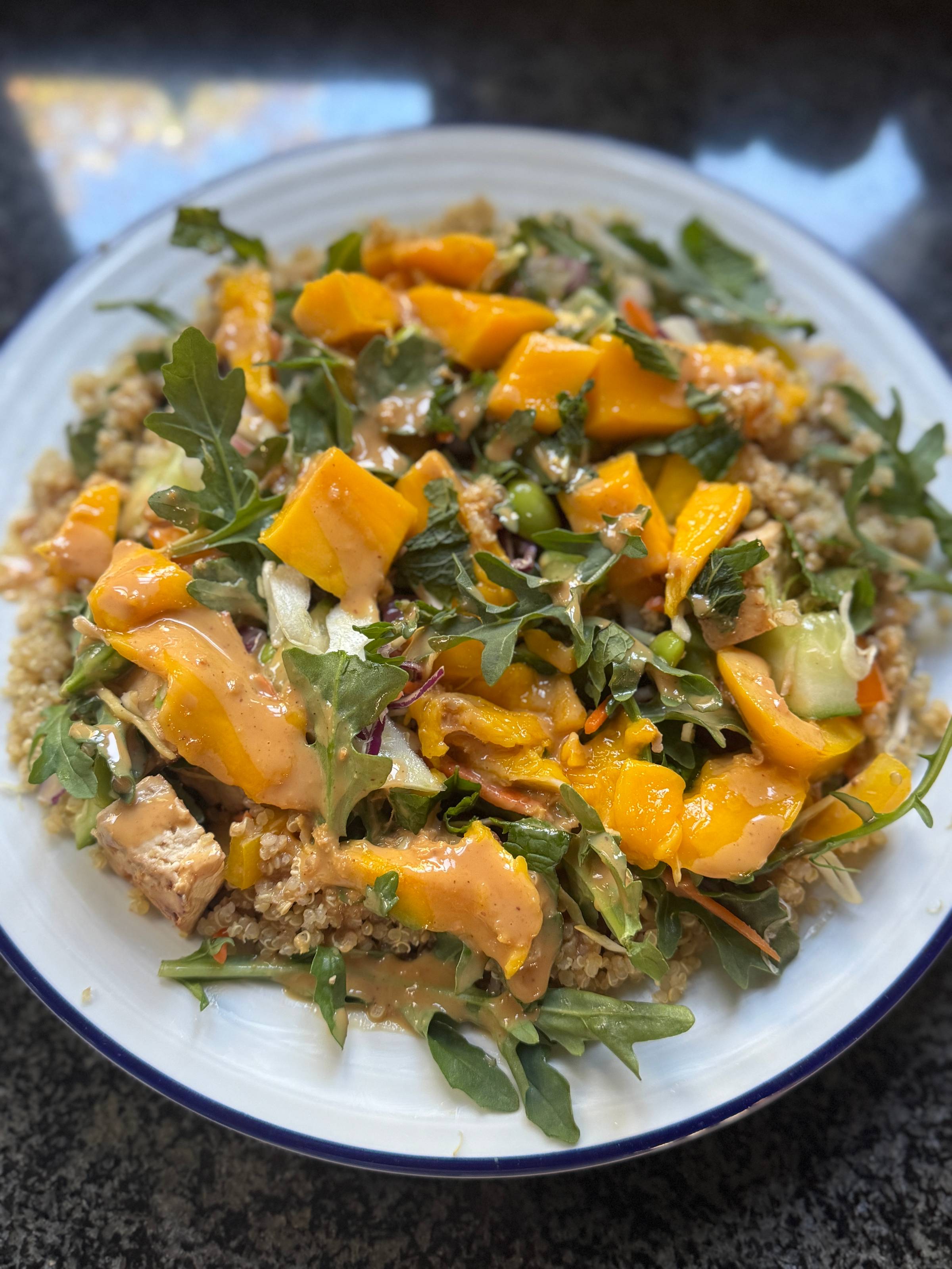 Quinoa bowl topped with fresh mango, arugula, cucumber, and herbs in a creamy peanut dressing