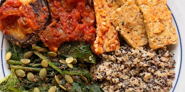 Colorful fresh vegetables and whole grains including red peppers, quinoa, and leafy greens on a wooden surface