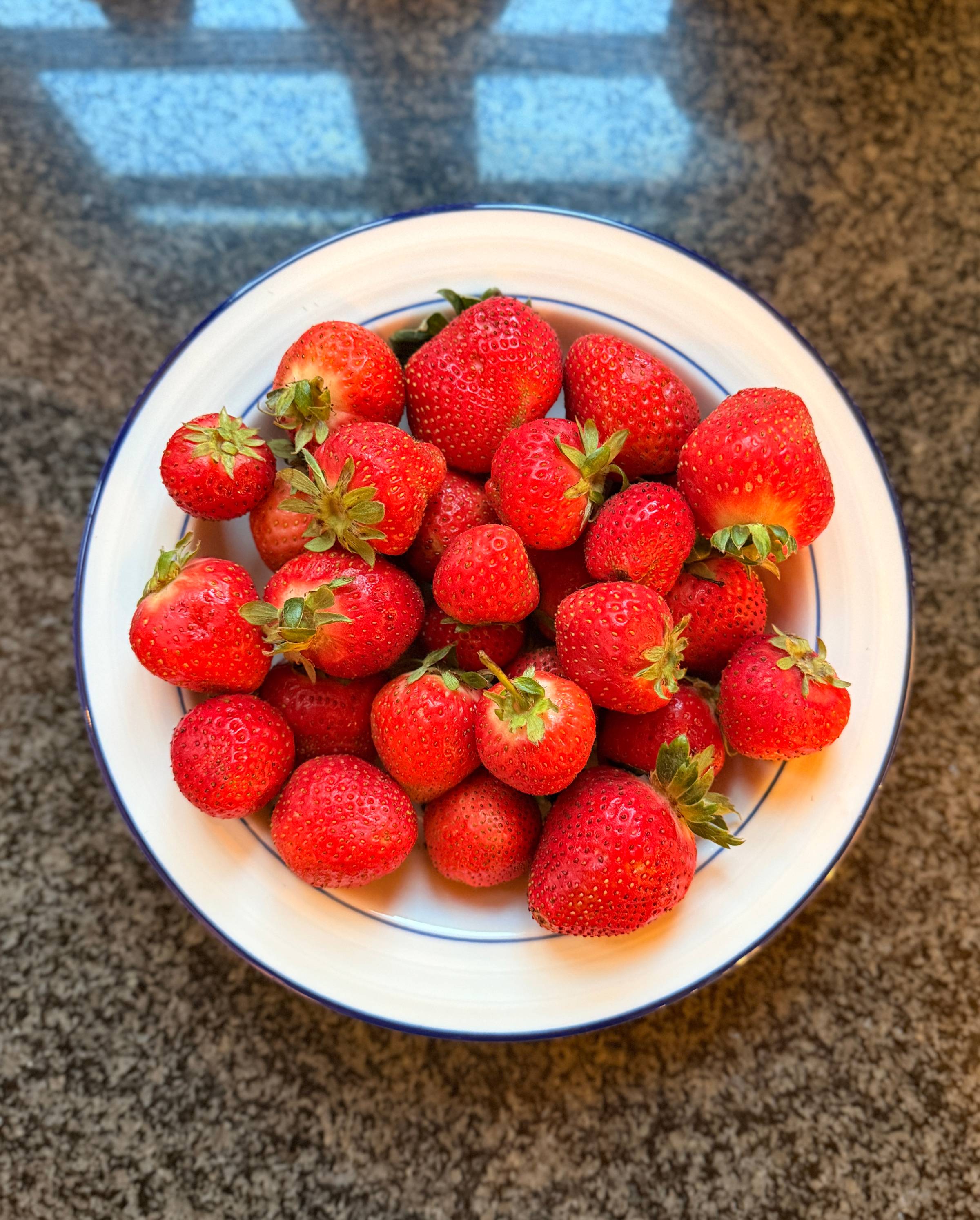 A white bowl filled with fresh ripe strawberries on a stone surface