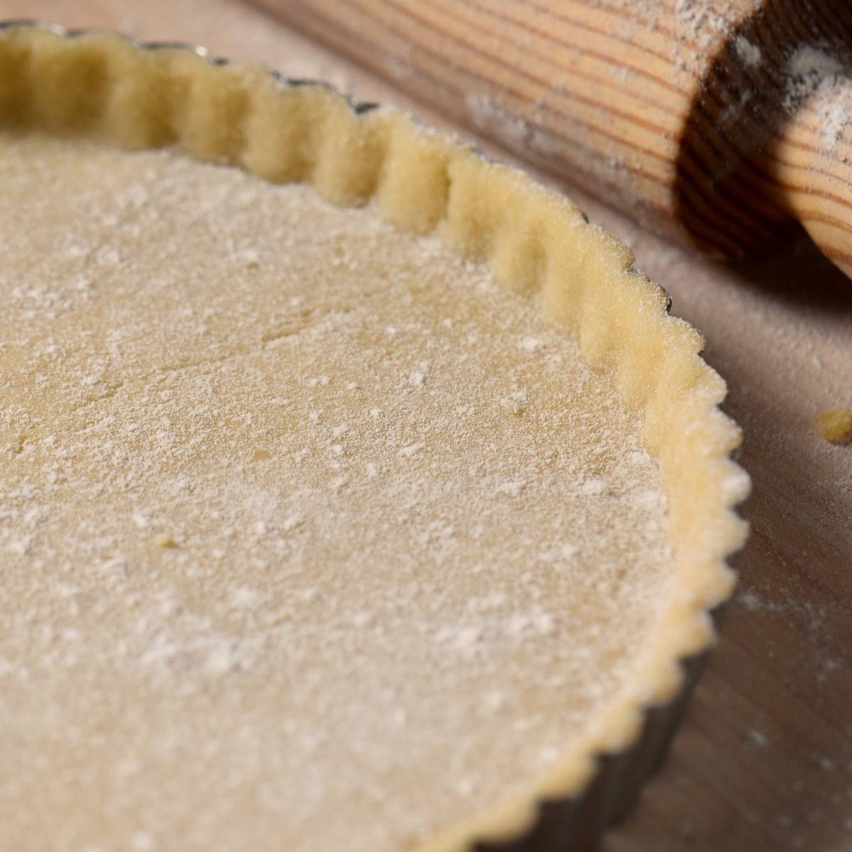 Pasta frolla crust next to a rolling pin.