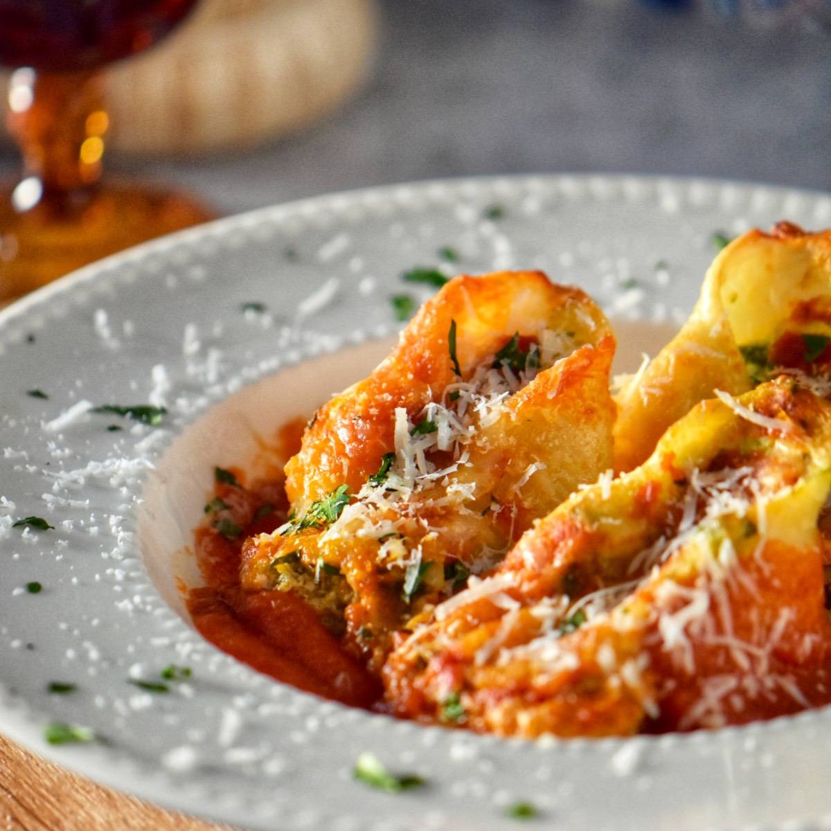 Three giant stuffed Italian pasta shells on a white dinner plate dusted with tomato sauce, grated cheese and chopped Italian parsley.