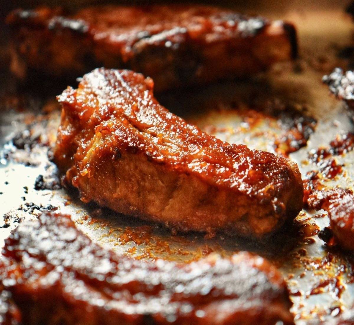 Oven baked ribs generously glazed with Bar-B-Barn sauce, resting on a baking pan.