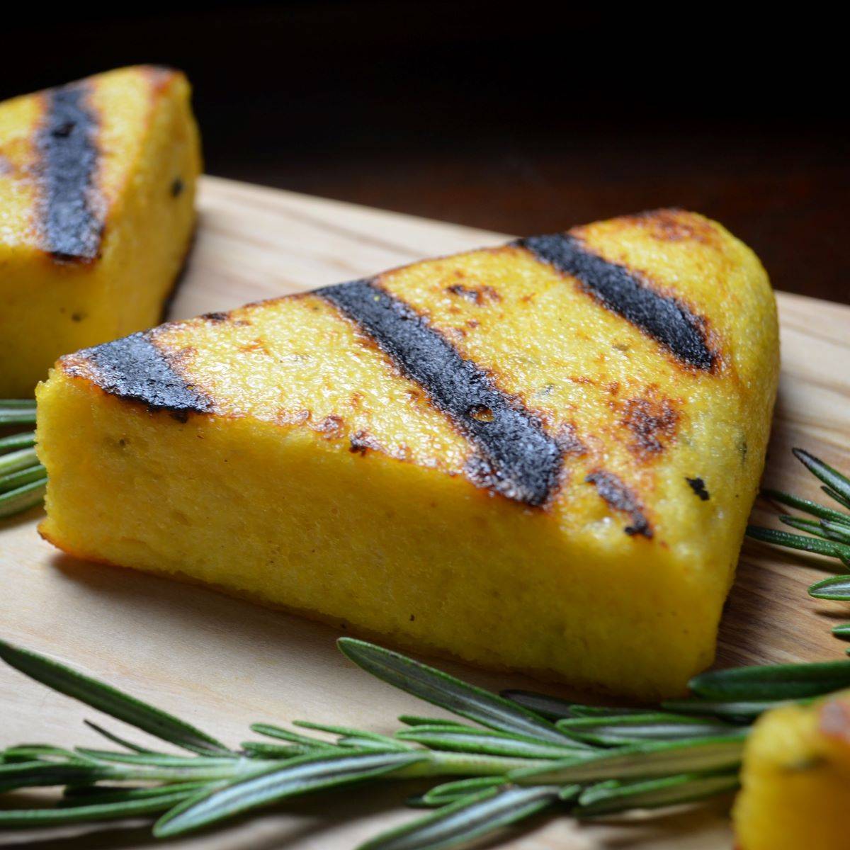 Grilled polenta next to a sprig of fresh rosemary.