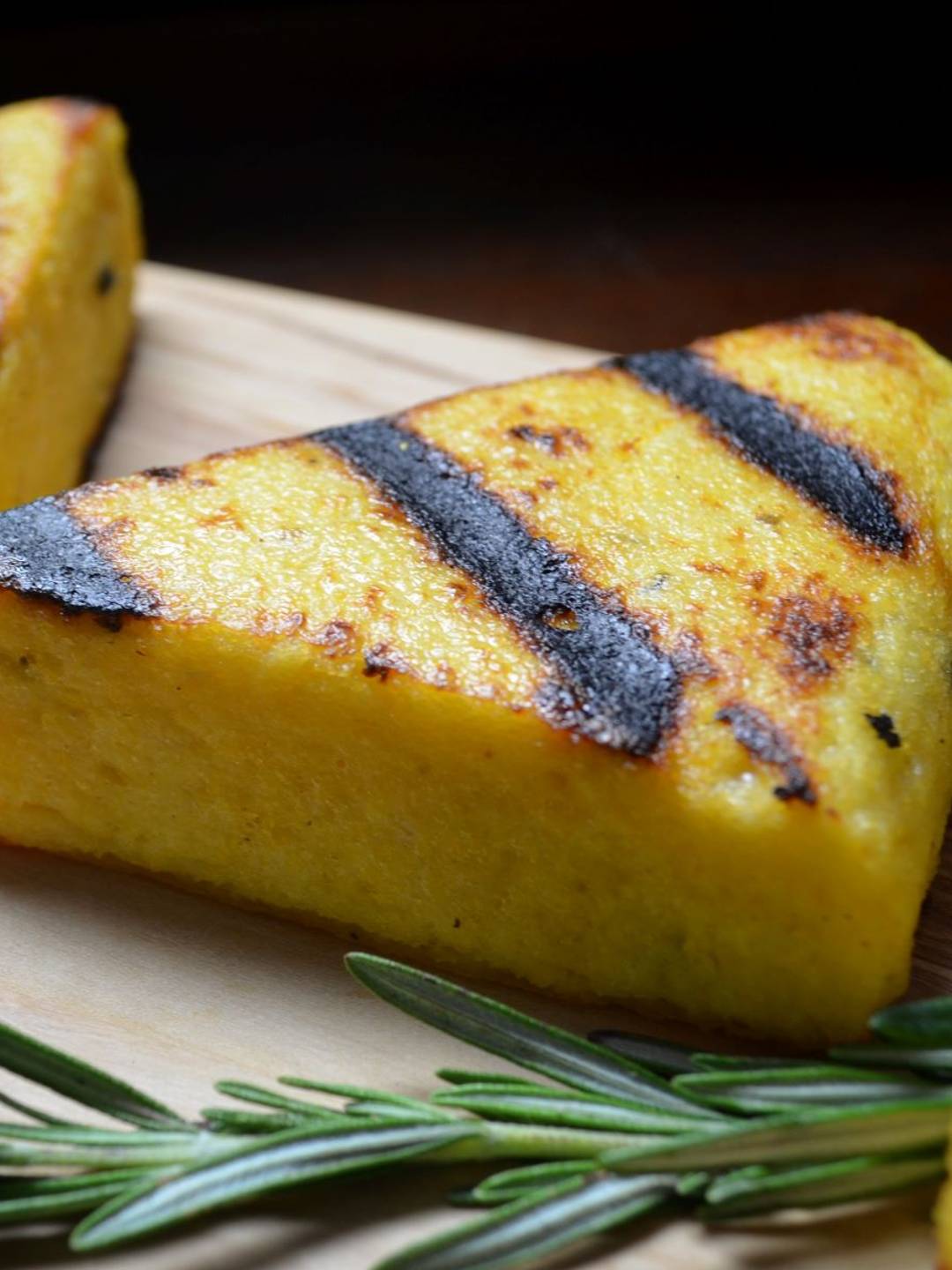 Grilled polenta next to a sprig of fresh rosemary.