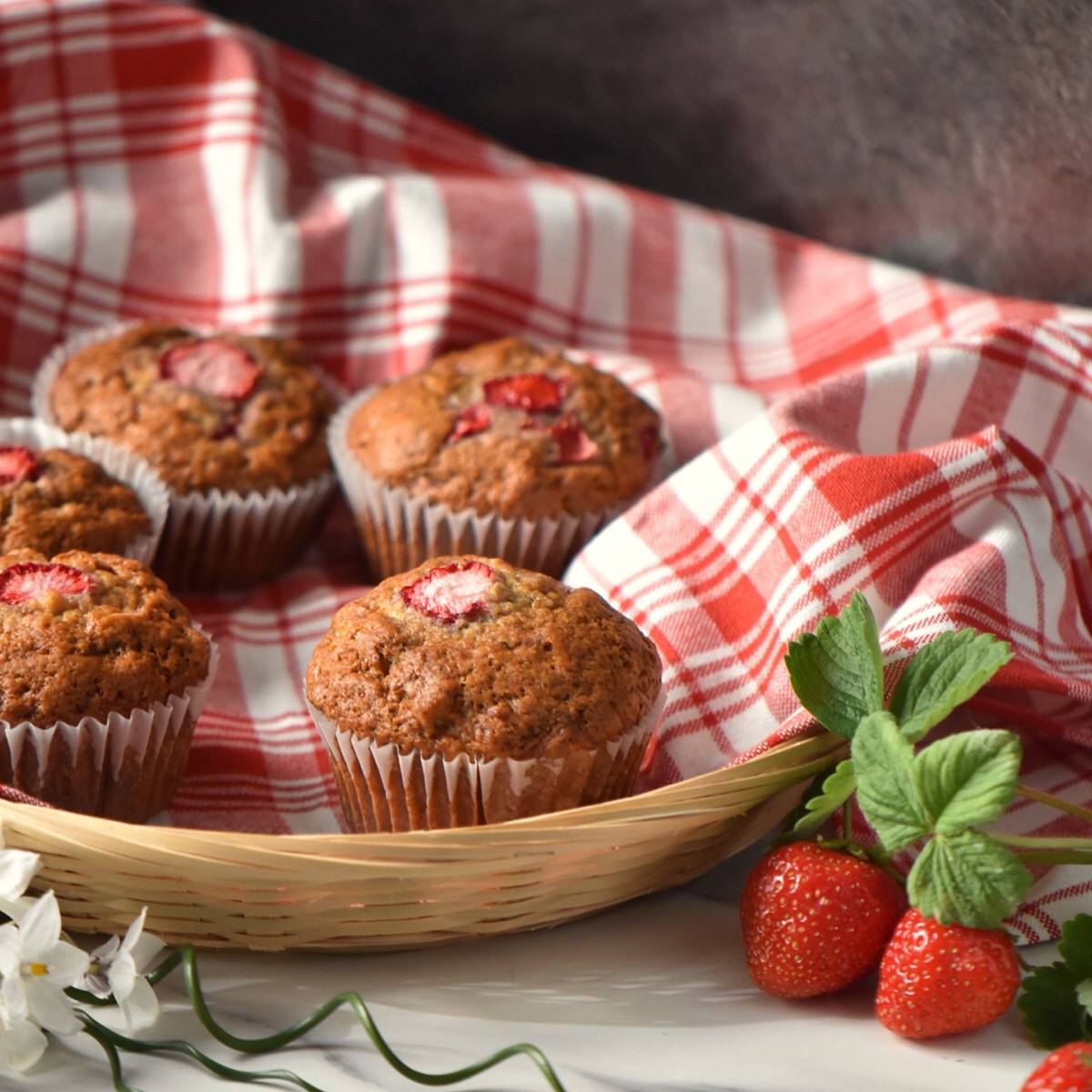 Banana muffins in a wicker basket surrounded by fresh strawberries.