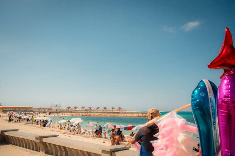 Sunny beach with people and a vendor holding balloons.