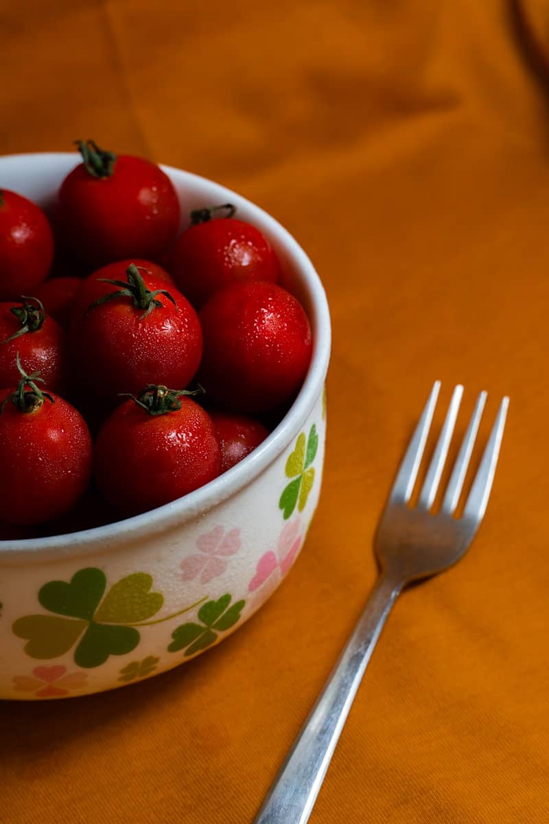 Wet cherry tomatoes in a patterned bowl with a fork.