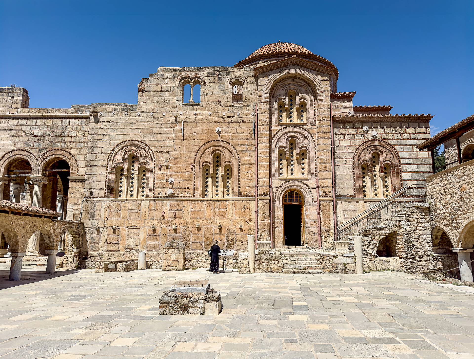 A lone woman figure standing at the side of a monumental Byzantine church
