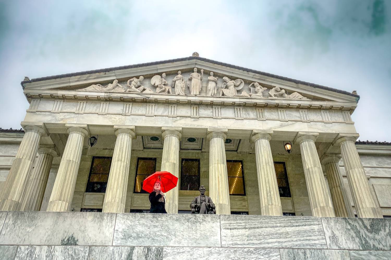 Woman in red umbrella standing infront of a history museum in the shape of a Classical Greek Doric Temple