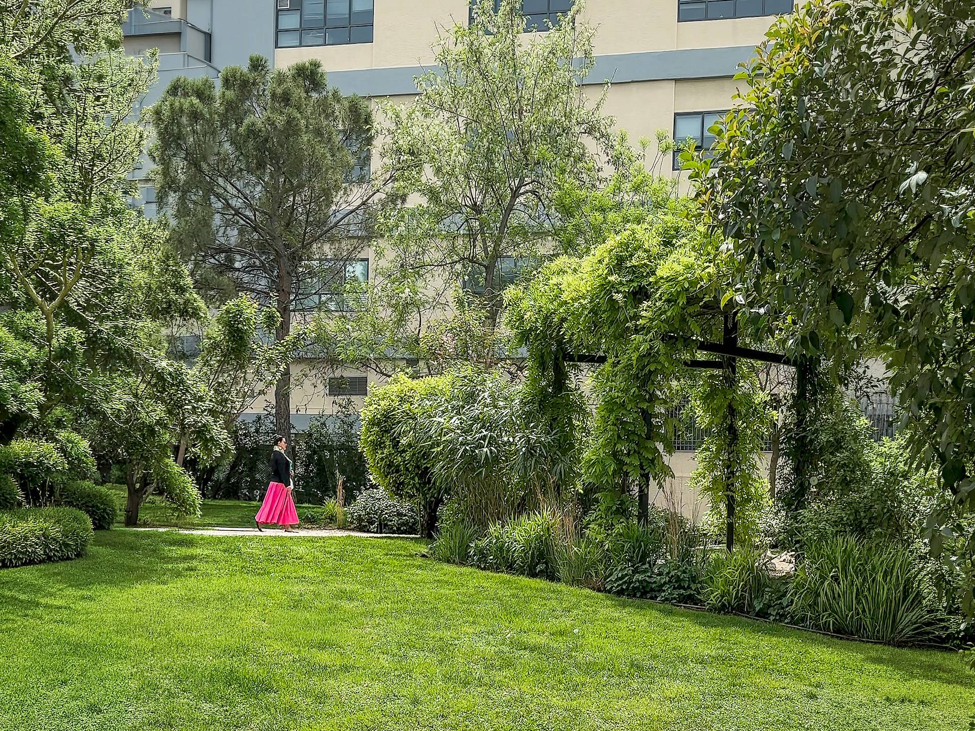Woman in pink dress walking the coblestone path of a verdant Japanese style park in a downtown rural environment