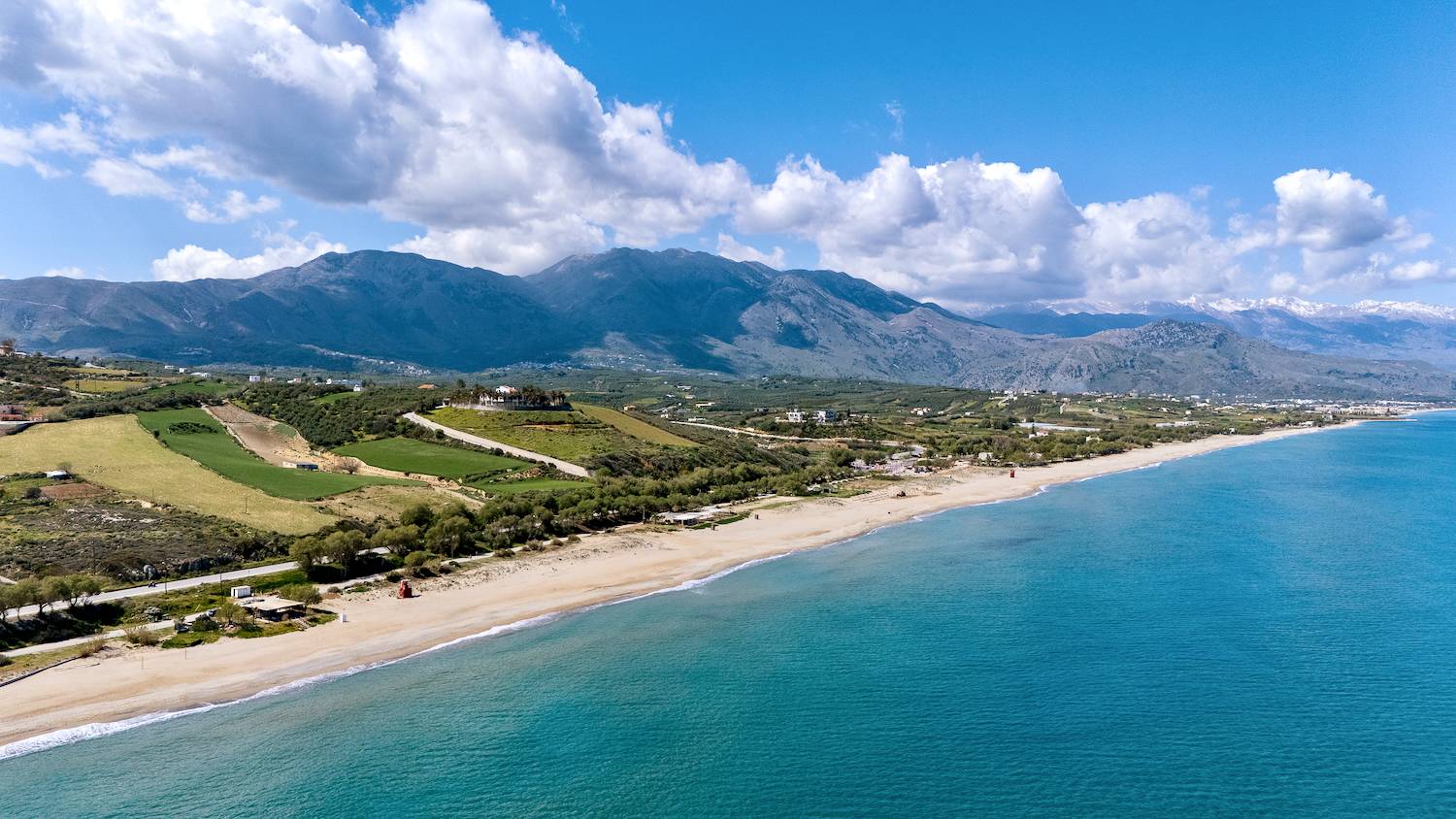 Dramatic coastline in Crete, with long beautiful sandy beach, azure seas and tall mountains with snow on the top in the background.