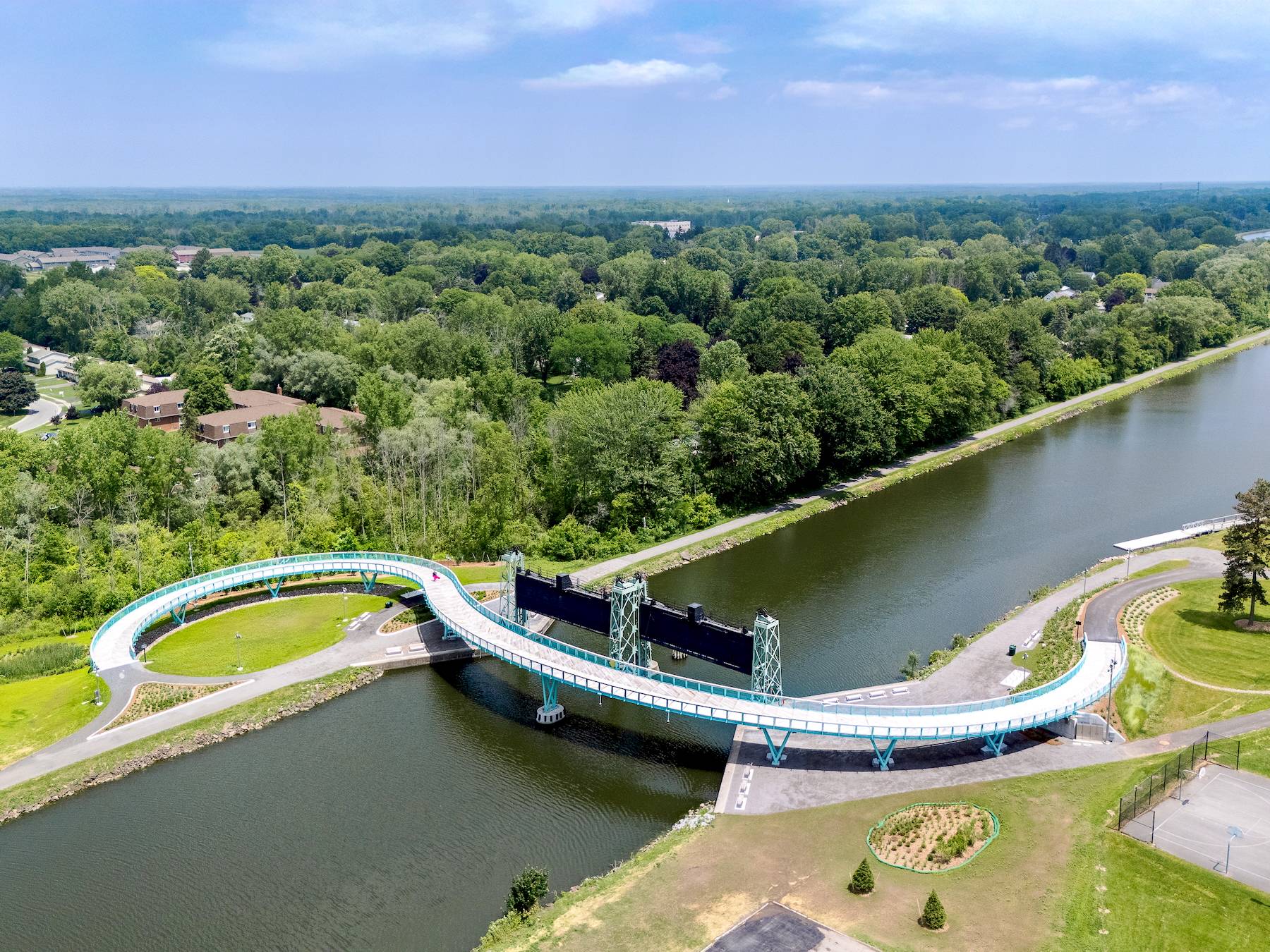 Aerial view of a modern S-shaped pedestrian bridge over the Erie Canal