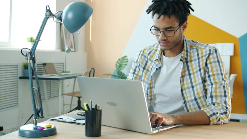 Man with dreadlocks working on laptop at desk.