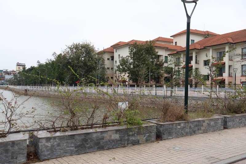 Apartment buildings line a calm river with trees.