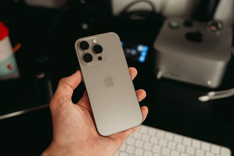 A hand holds an iPhone with triple cameras.