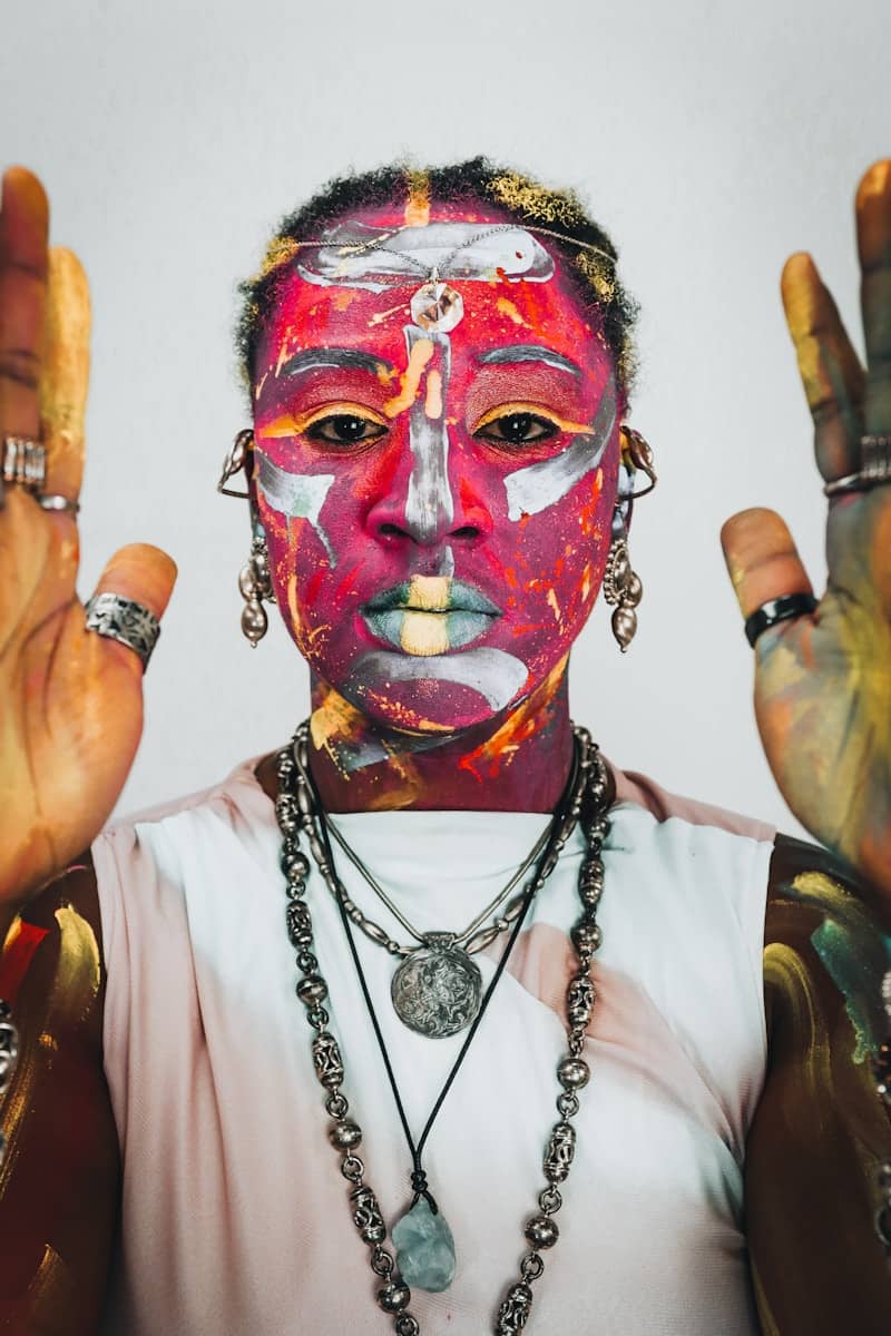 Person with vibrant face and body paint, hands raised.
