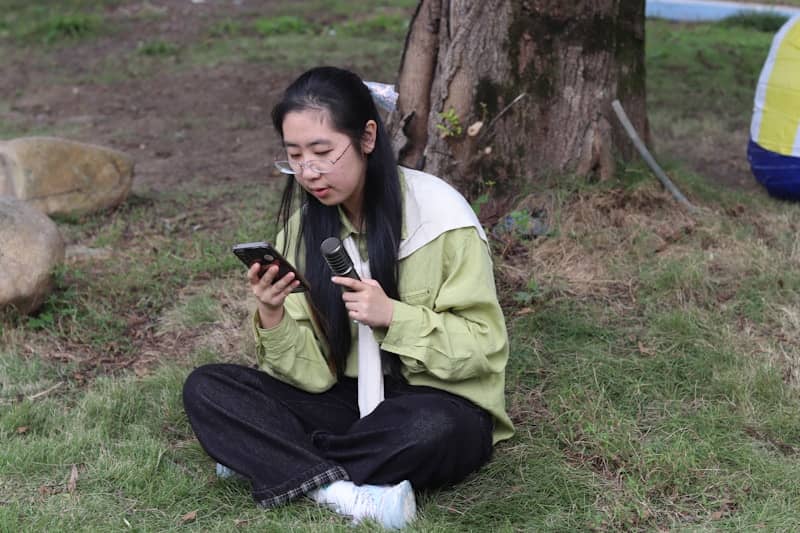 A young woman sitting on grass, looking at her phone.
