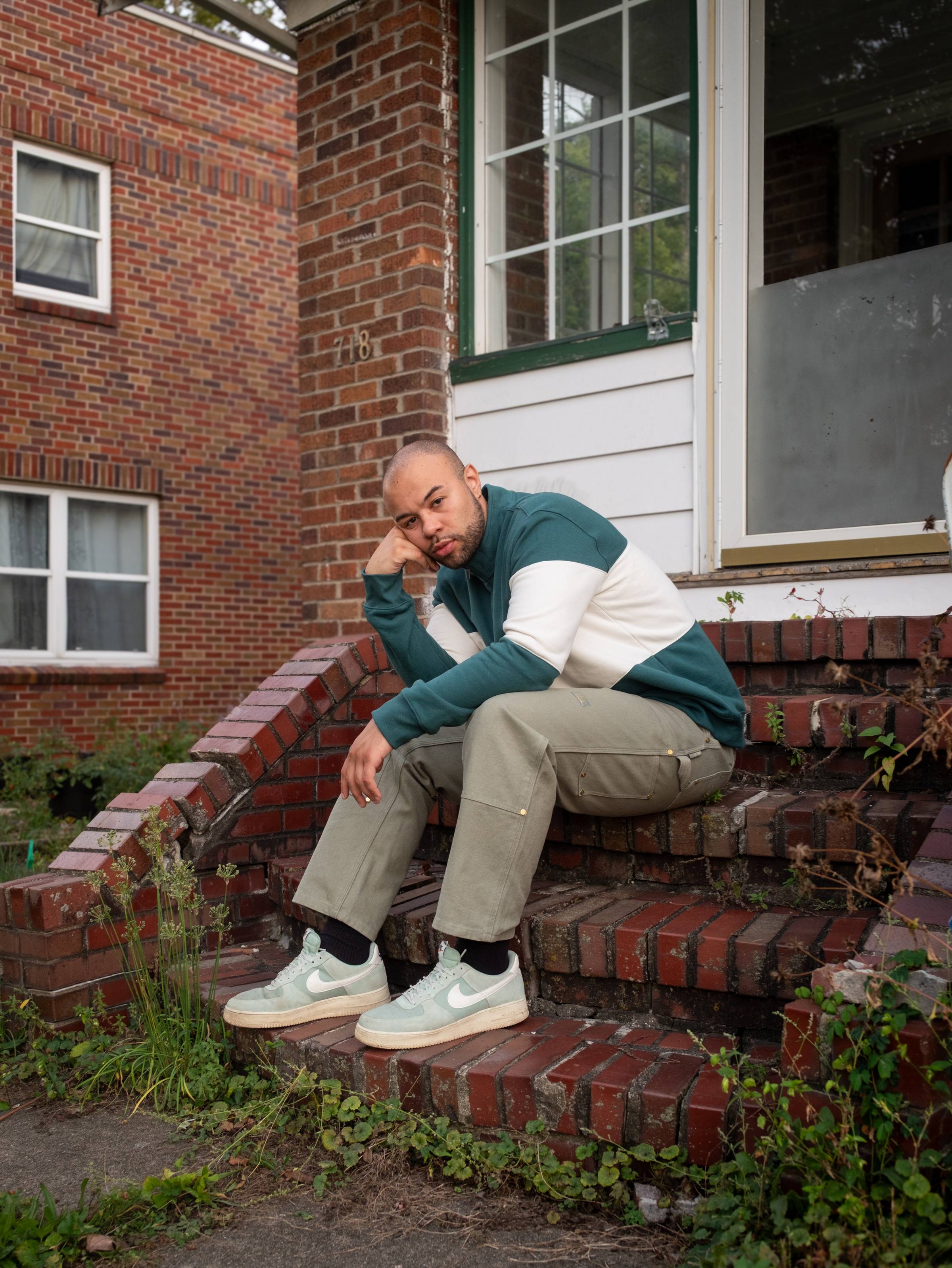 a light skinned Black man sits on a stoop outside