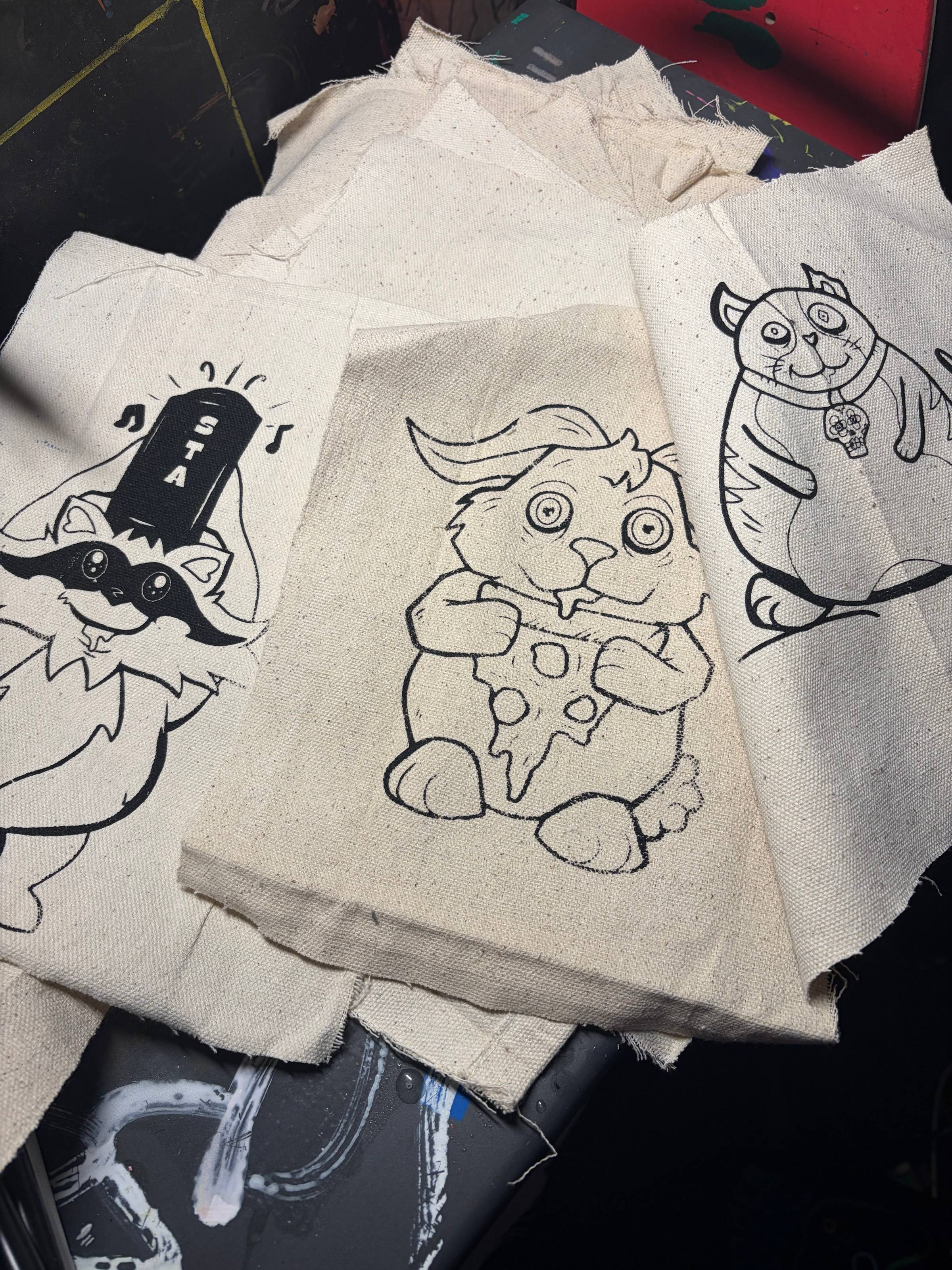 small rectangle of canvas with a black outline print of the MONfest characters raccoon, bunny, and cat