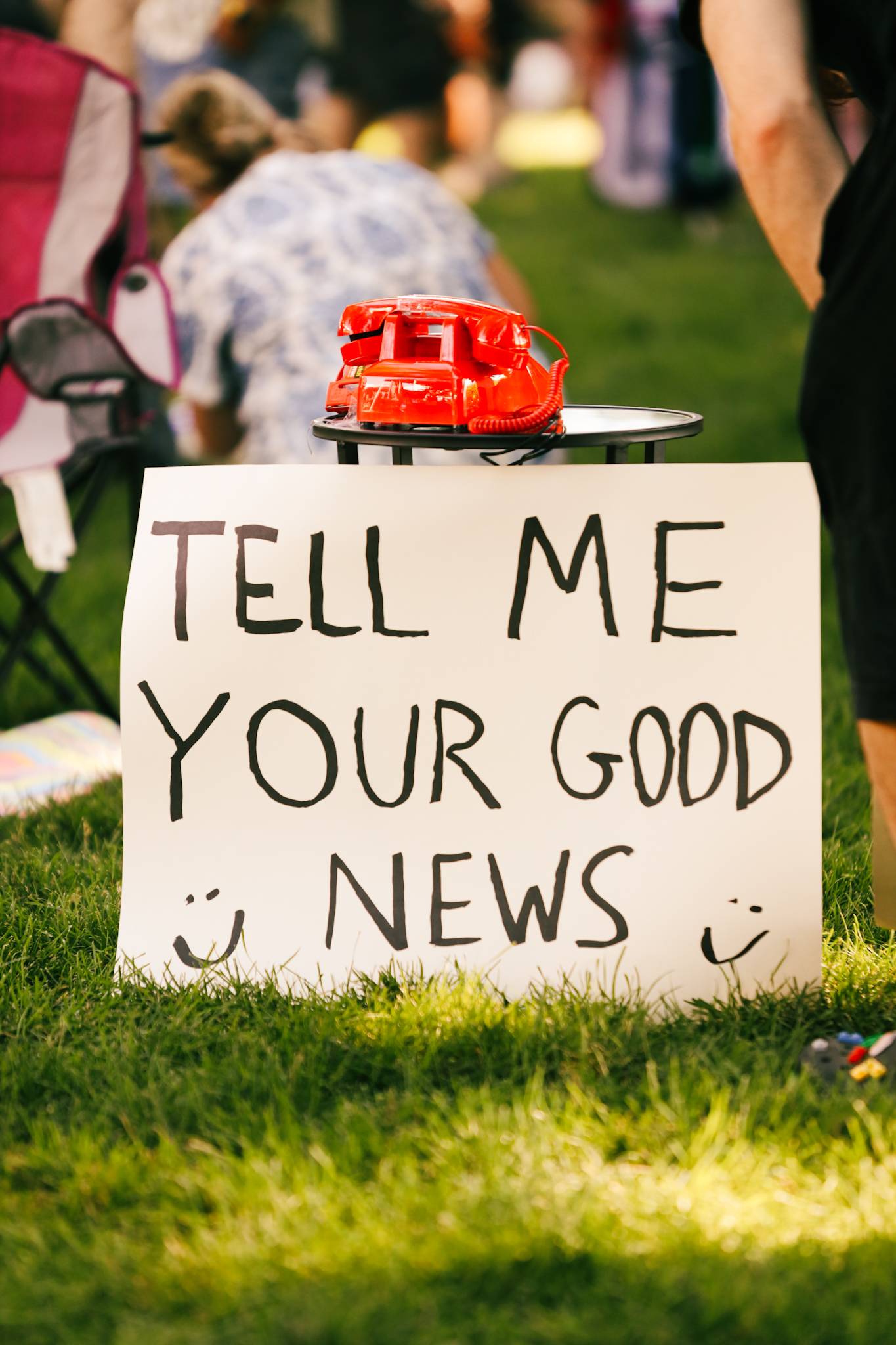 a handwritten sign that reads "tell me your good news" under a red vintage telephone