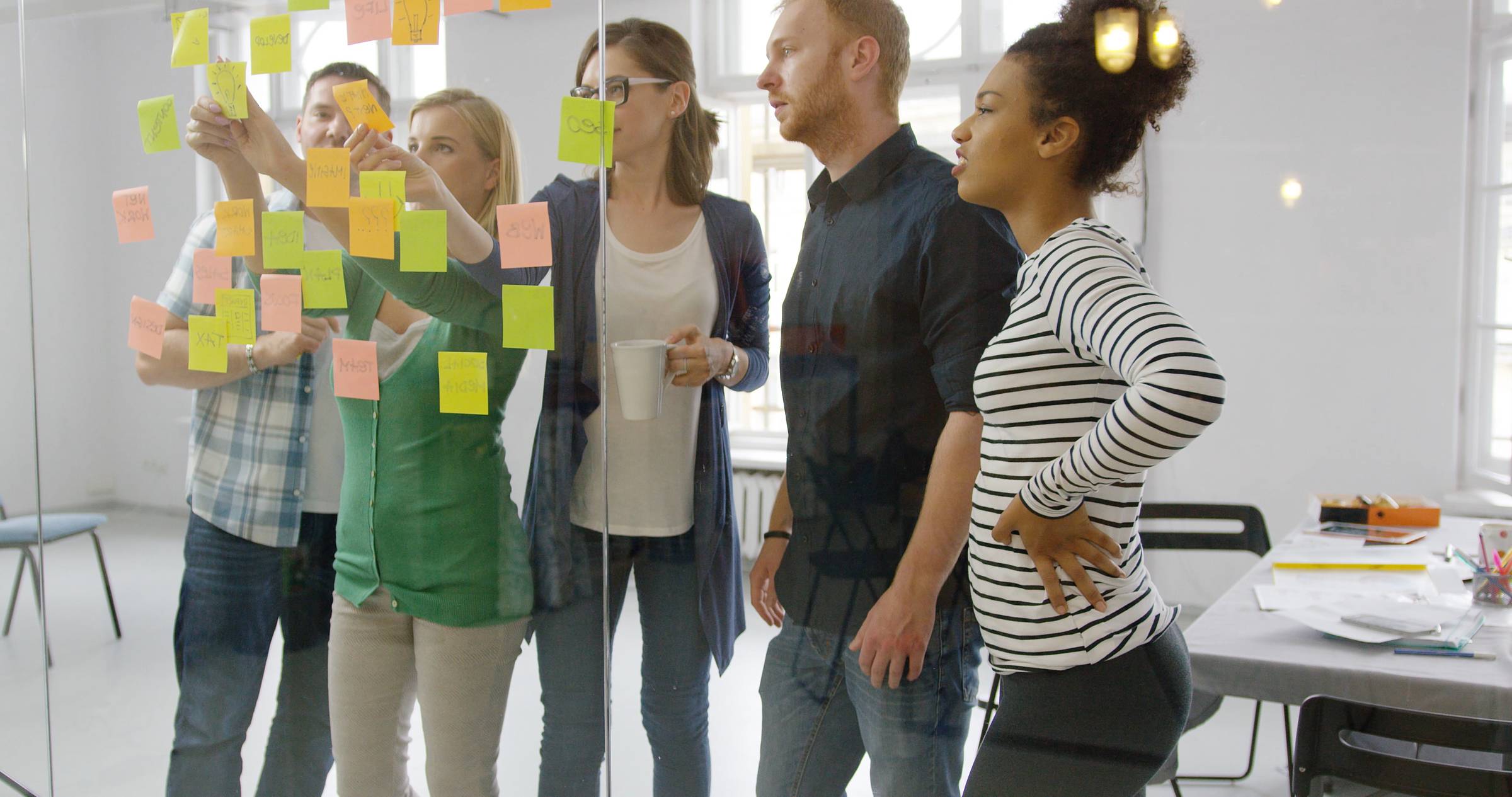 Group of young professionals gathered around a glass wall covered in multi-coloured Post-it notes.