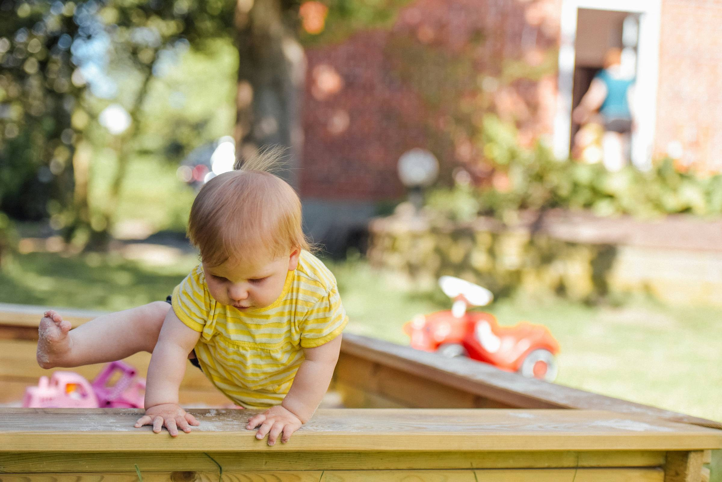 Baby climbing out of a sandpit