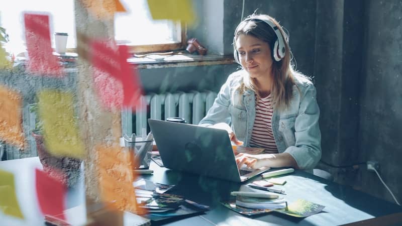 A woman is working on her laptop headphones on writing music.