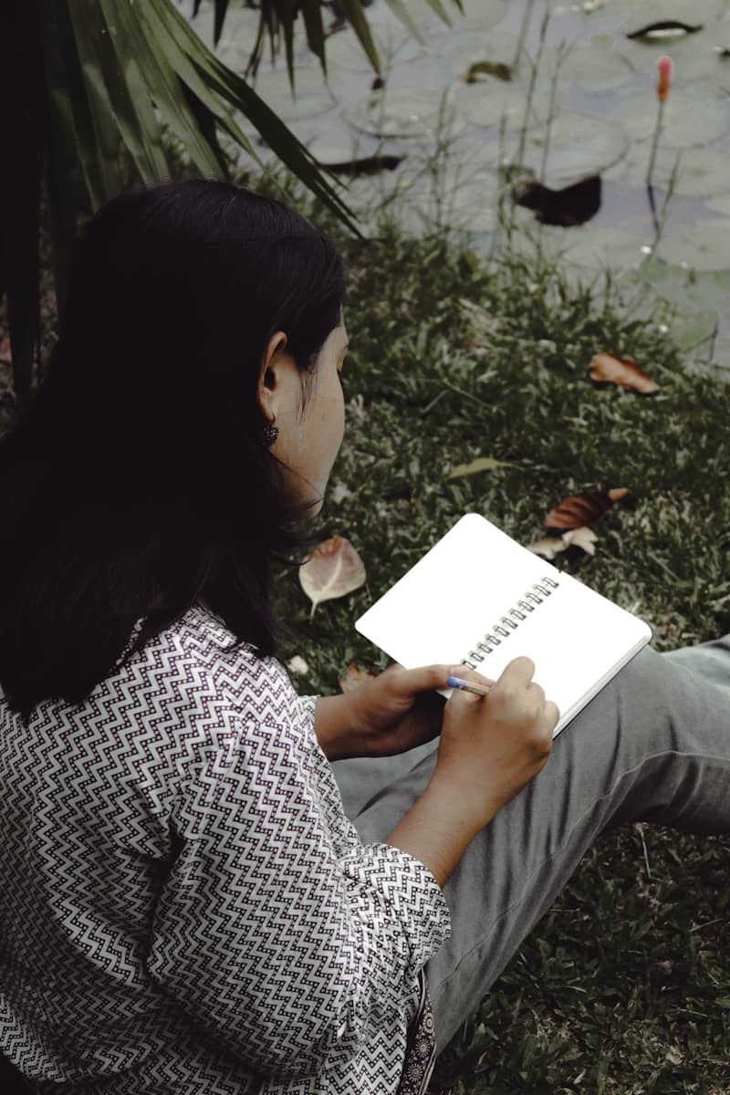 Woman writes in her notebook outdoors by the water.