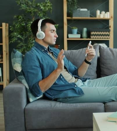 Man wearing headphones listens to music on couch.