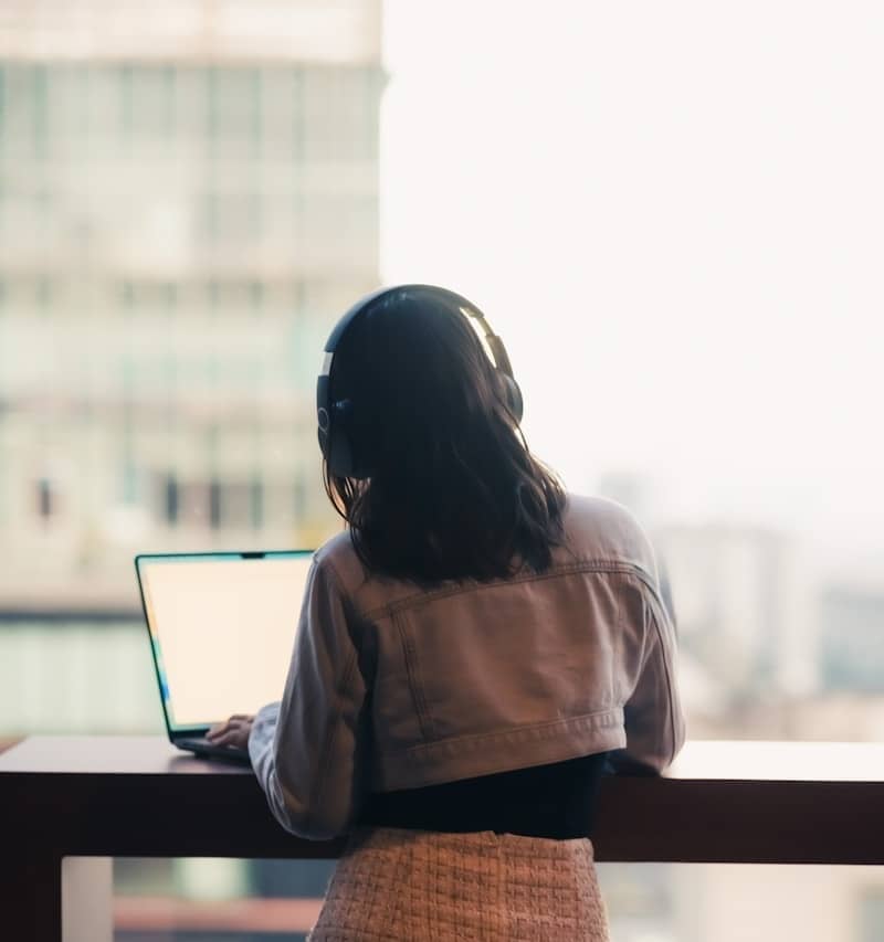 Woman with headphones using laptop by window
