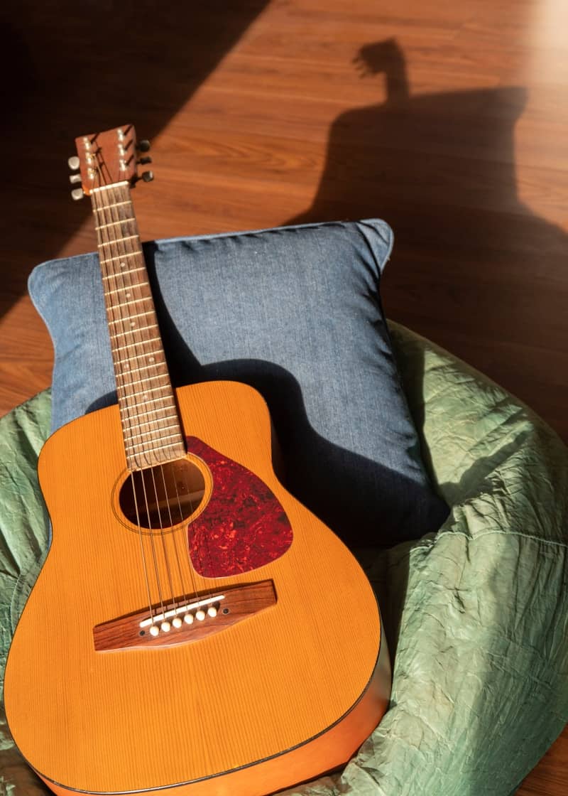 An acoustic guitar rests on a pillow.