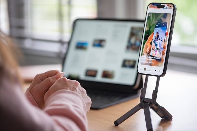 Hands near phone on tripod displaying social media, tablet behind.