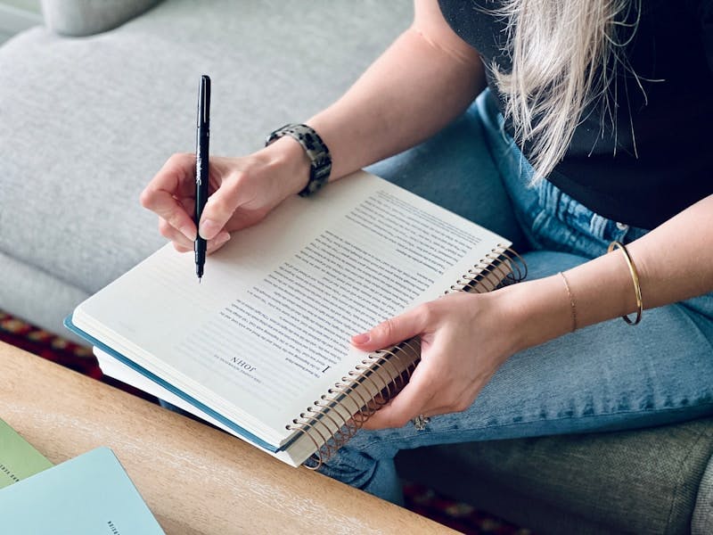 a woman sitting on a couch writing on a notebook