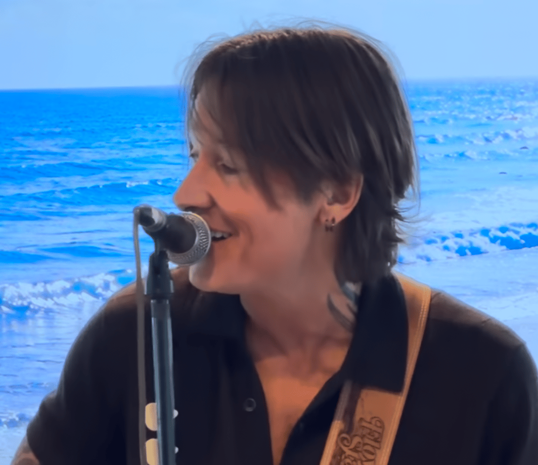 keith urban sings into a mic with the ocean waves behind him