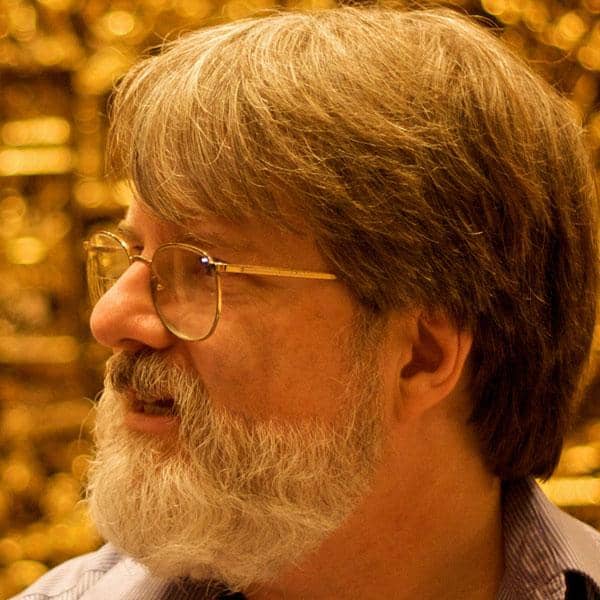 Man with grey hair and glasses looks off into the distance, thoughtfully