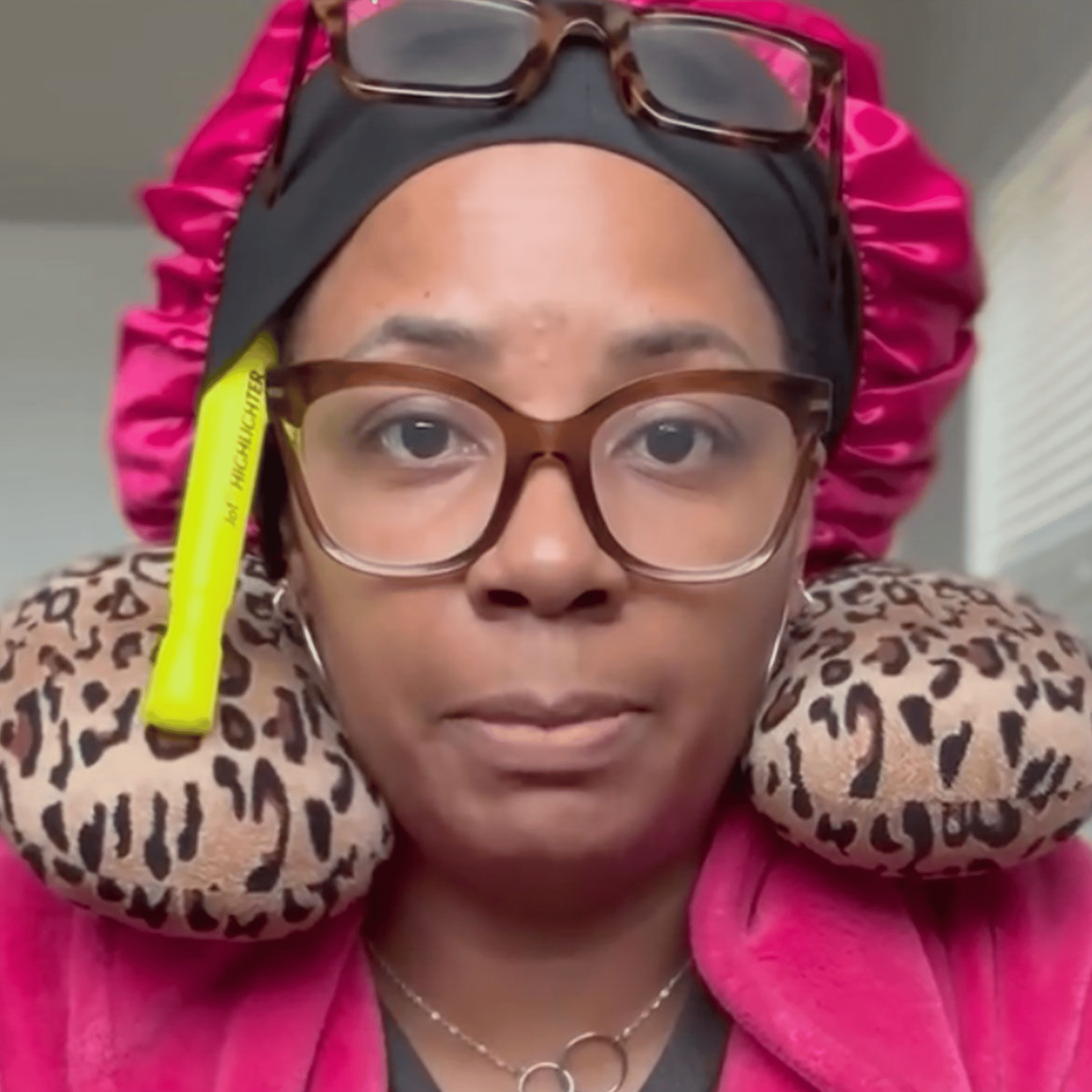 woman is wearing glasses and also has another pair on her forhead; she has a travel pillow around her neck and a highlighter sticking out of her headband