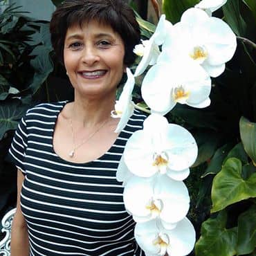 Malini Schueller stands behind a gorgeous, white, blooming orchid vine