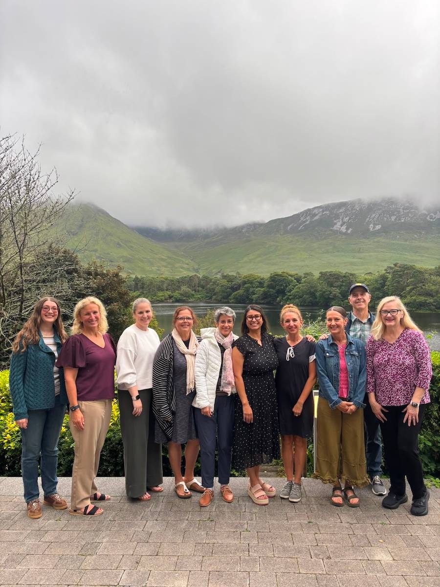 Group of ten stand for a group photo in front of a lake