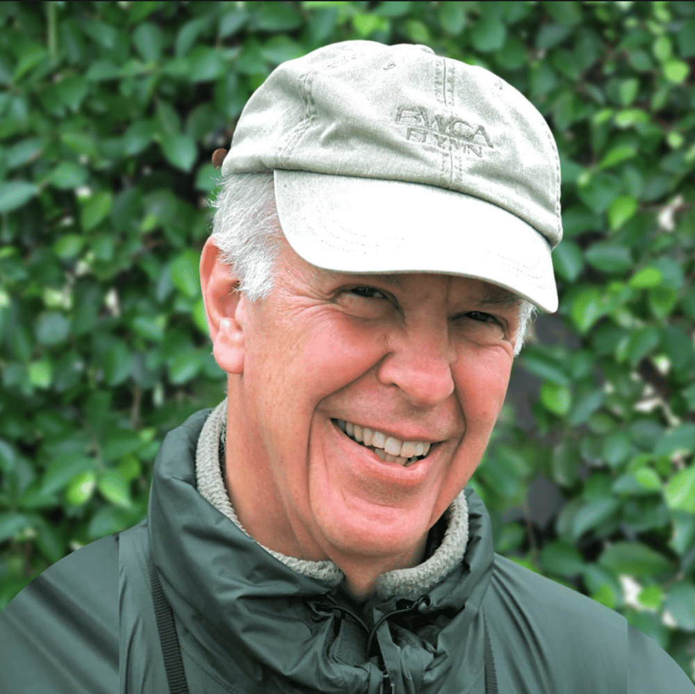 man wearing a hat and a windbreaker smiles warmly