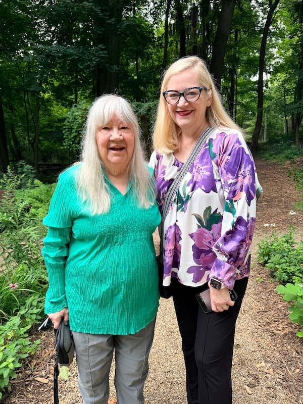 Two women stand together in a lush garden