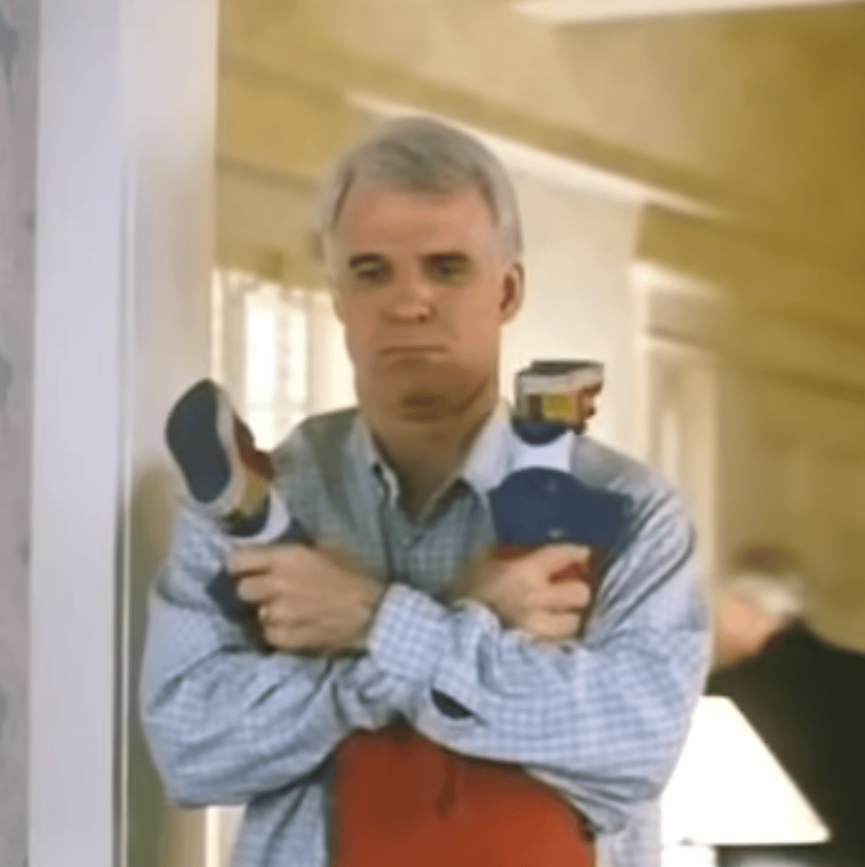 Steve Martin holds a child upside down (all we see are the child's feet, near Steve's head. He looks discouraged.