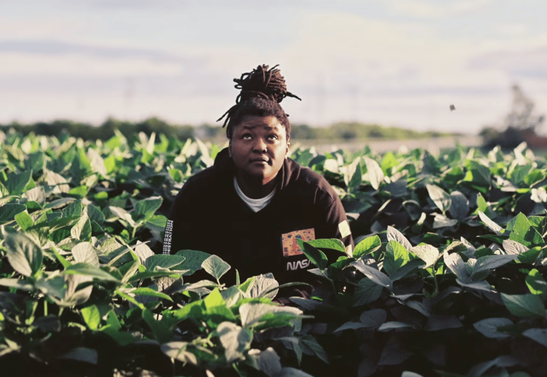 Joy Oladokun has a contemplative look on her face. She's surrounded by greenery and is looking up at the sky.