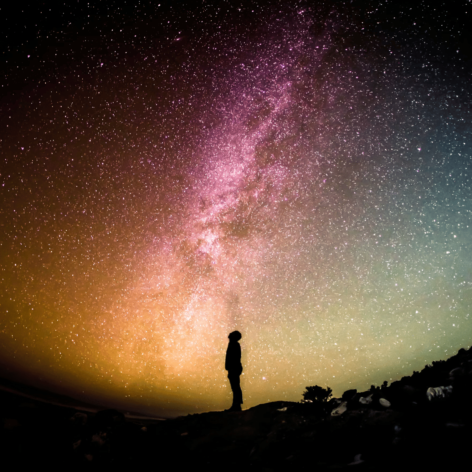 Distant silhouette of a person looking at an expansive s full of stars and light. ky