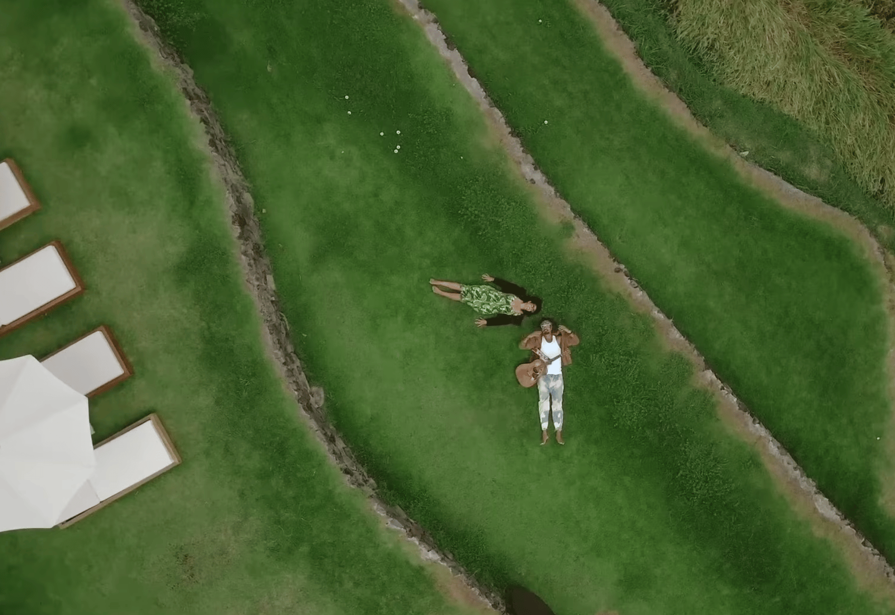 Woman and man lay on their backs on the grass. We see them from an aerial view.