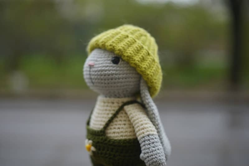 A crocheted bunny wearing a green hat and overalls